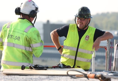 Tvä byggnadsarbetare står och pratar iklädda arbetskläder