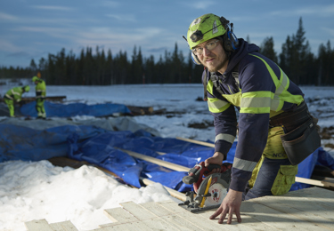 Byggnadsarbetare som sågar i trä med cirkelsåg