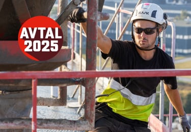 Byggnadsarbetare med skyddshjälm och solglasögon arbetar på en byggställning i solen. Han hanterar en stor betongstruktur med ena handen. I bakgrunden syns byggnadsställningar och ett landskap. En röd cirkel med texten 'AVTAL 2025' är placerad i bilden.