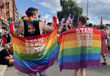 Två personer iklädda Stark, Stolt, Trygg vepor står tätt tillsammans på plats i tåget.