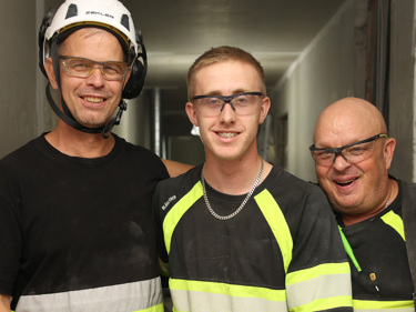 Tre byggnadsarbetare tittar in i kameran