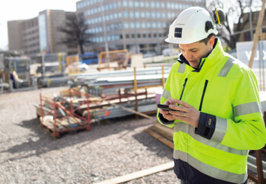 En person i hjälm, varseljacka och med en mobil i handen.