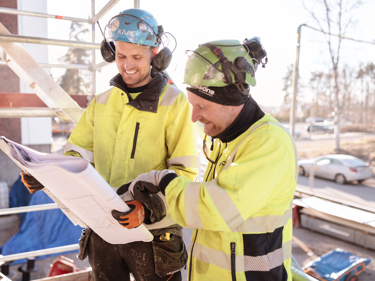 2 byggnadsarbetare studerar ritningar på ett bygge