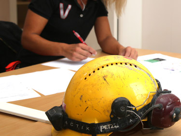 Person skriver på papper med penna med en bygghjälm i förgrunden