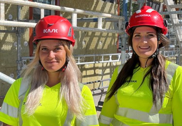 Två kvinnliga byggnadsarbetare i hjälm och varseltröja.