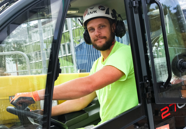 Byggnadsarbetare med hjälm sitter i en gaffeltruck