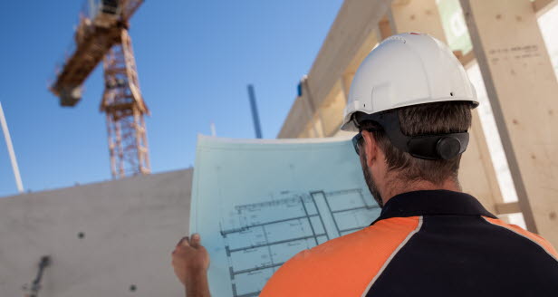 Person tittar på ritningar på en byggarbetsplats med en kran i bakgrunden.