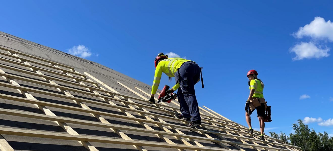 Två kvinnliga byggnadsarbetare jobbar på ett tak.