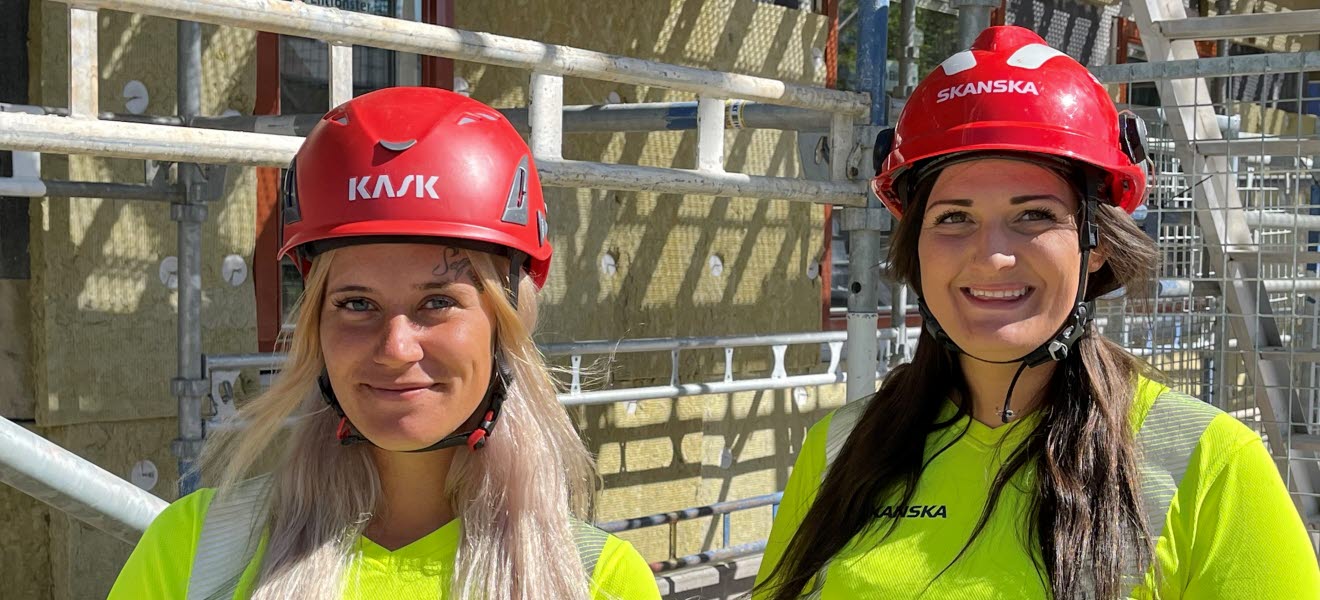 Två kvinnliga byggnadsarbetare ler.