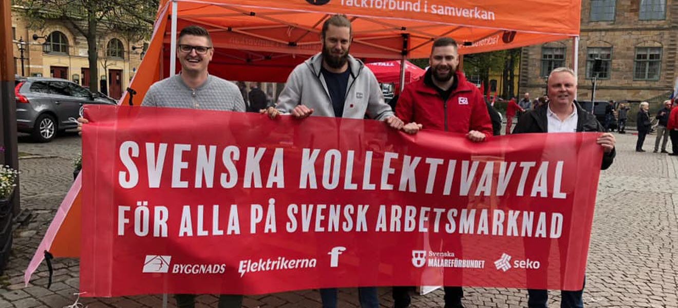 Fyra personer håller en banderoll med texten Svenska kollektivavtal för alla på svensk arbetsmarknad